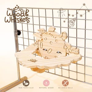 May include: A light-colored wooden platform for small animals featuring a circular back panel with engraved flower and cloud motifs. The platform is attached to a metal grid. Text includes The Wood & Whiskers, Non-toxic glue, Natural wood, No-screw nails.