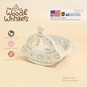 May include: A light-colored wooden pet bed shaped like a spaceship, with heart and star cutouts. The bed is made from kiln-dried pine and features the text "The Wood & Whiskers". It is constructed with non-toxic glue and no-screw nails.