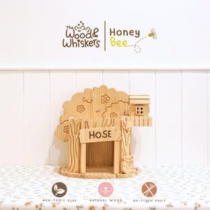 Puede incluir: Una casa en el árbol de madera con un letrero que dice "HOSE". La casa en el árbol tiene una pequeña casa en una rama y está decorada con detalles tallados. La imagen también incluye el texto "The Wood & Whiskers Honey Bee".
