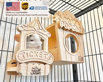 May include: A light-coloured chinchilla looks out from a wooden ticket booth-shaped structure. The booth has the word "TICKETS" carved on it. Next to it is a wooden house with a "POPCORN" sign. The structures are inside a wire cage.