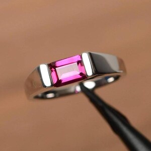 May include: A silver ring with a rectangular, bright pink gemstone. The ring has a modern design with a polished finish, showcasing the gemstone prominently. The setting is sleek and minimalist, highlighting the stone's colour and shape.