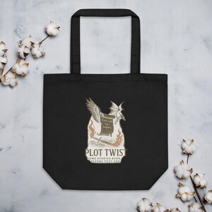 May include: Black tote bag with a fantasy design. The graphic includes a dragon, wings, a sword, and flames, with the words "PLOT TWIST" and "Every oath has a loophole." The bag is made of a durable material.