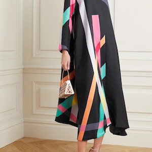 Può includere: Abito midi nero con un motivo geometrico colorato in rosa, arancione, verde e bianco. L'abito ha maniche lunghe e scollo a V. Viene tenuta una piccola borsa geometrica dorata. La persona indossa sandali con tacco alto.