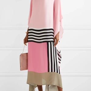 May include: A flowing pink dress with a color block design featuring black and white stripes and a pink and tan panel. The dress has long, wide sleeves and is paired with rose gold heels and a matching purse.