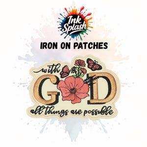 May include: An iron-on patch with the text "with God all things are possible." The patch features a floral design with a large pink flower, butterflies, and the letters "G" and "D" in a gold colour. The words "Ink Splash" and "IRON ON PATCHES" are at the top.