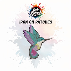 May include: Embroidered iron-on patch of a hummingbird in flight, with teal, purple, and pink colours. The patch has a black border and is set against a watercolour splash background. Text at the top reads "Ink Splash" and "IRON ON PATCHES".