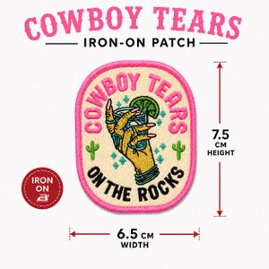 May include: An oval iron-on patch featuring a yellow hand holding a glass with a lime slice. The text reads COWBOY TEARS ON THE ROCKS. It includes small green cactus icons and blue sparkles. The patch measures 7.5 cm in height and 6.5 cm in width.