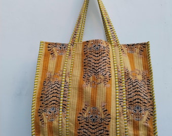 May include: A large tote bag with a tiger print. The bag features a repeating pattern of tiger faces and stripes in shades of orange, black, and yellow. The bag has matching handles and trim.