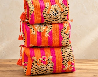Könnte beinhalten: Ein Stapel aus drei rechteckigen, gesteppten Taschen mit vertikalen orangefarbenen und pinken Streifen sowie einem Tiger-Muster. Jede Tasche hat einen Reißverschluss und eine dekorative orangefarbene Quaste am Zipper.