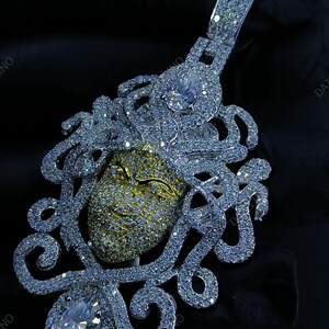 May include: A dazzling pendant featuring a Medusa design. The pendant showcases a gold-toned face, intricately detailed with sparkling white gemstones. The design includes flowing, ornate details and a large, clear gemstone at the bottom.