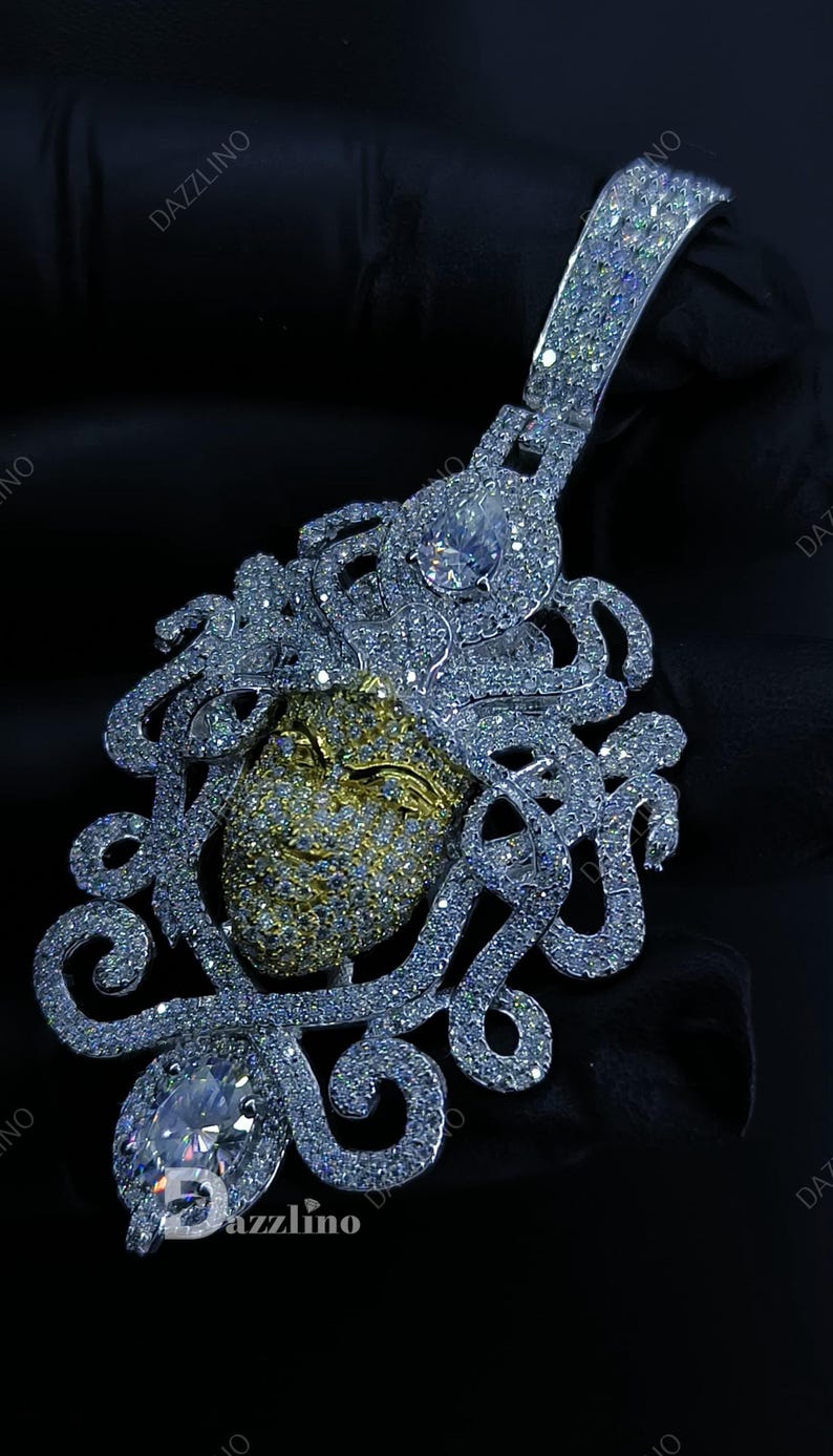 May include: A dazzling pendant featuring a Medusa design. The pendant showcases a gold-toned face, intricately detailed with sparkling white gemstones. The design includes flowing, ornate details and a large, clear gemstone at the bottom.