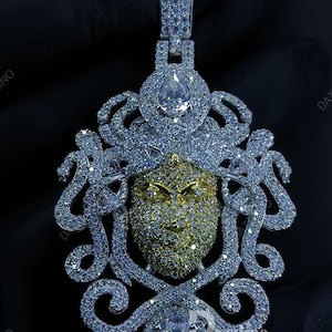 May include: A dazzling pendant featuring a Medusa-like face design. The pendant is encrusted with sparkling gemstones in silver and gold tones. The design includes a large central stone and intricate detailing.