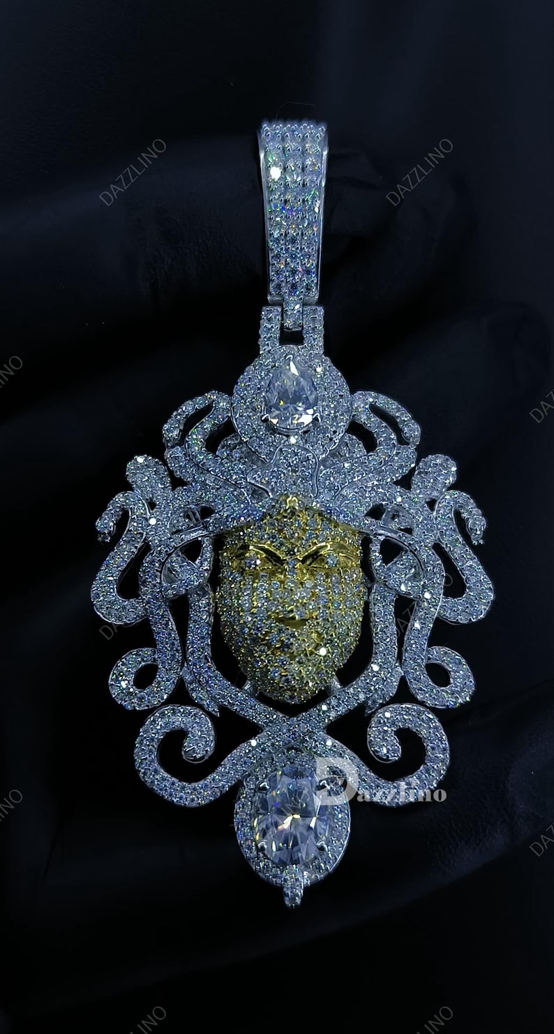 May include: A dazzling pendant featuring a Medusa-like face design. The pendant is encrusted with sparkling gemstones in silver and gold tones. The design includes a large central stone and intricate detailing.