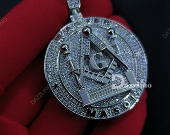 May include: A silver-colored pendant with a round design, featuring a Masonic symbol with the letters "G" and "MASON". The pendant is encrusted with small, sparkling stones and has a bail for a chain.