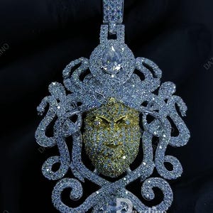 May include: A dazzling pendant featuring a gold-toned face with intricate detailing, surrounded by a silver-colored, ornate design. The pendant is encrusted with numerous sparkling stones, creating a luxurious and eye-catching piece of jewelry.