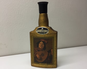 May include: A gold-colored glass bottle with a black plastic stopper. The bottle has a label that says "Beam's Choice 4/5 Quart". The bottle has a picture of a man playing a lute.