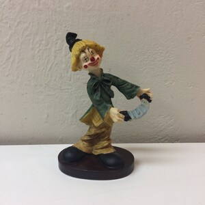 Vintage bisque clown figurine on a wooden stand playing a concertina with a smile.