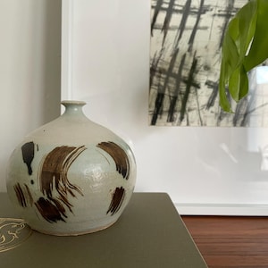 May include: A white ceramic vase with brown brushstrokes and black accents. The vase has a rounded body and a narrow neck.
