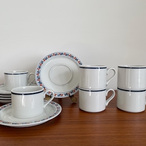 May include: Set of six white ceramic coffee cups with blue and red floral trim. The cups are stacked in pairs and are on matching saucers.