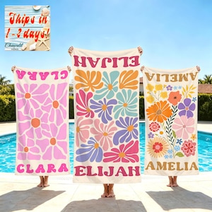May include: Three rectangular beach towels featuring personalized names and floral patterns. The left towel is pink and white with the name CLARA. The center towel has multicolored flowers and the name ELIJAH. The right towel has various flowers and the name AMELIA.