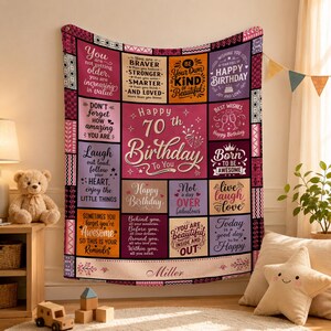 May include: A rectangular throw blanket featuring a patchwork design with various inspirational quotes and birthday messages in shades of pink, purple, orange, and white. The center text reads Happy 70th Birthday To You, with the name Miller at the bottom.