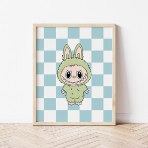 May include: A framed print featuring a cartoon character in a green bunny costume with a menacing grin. The background is a blue and white checkered pattern. The artwork is displayed in a light-colored wooden frame.