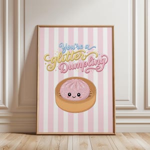 Könnte beinhalten: Ein gerahmter Kunstdruck mit einem Hintergrund aus rosa und weißen vertikalen Streifen. Der Text lautet You're a glitter Dumpling in blauer, gelber und rosa Schrift. Darunter ist ein rosa Cartoon-Dumpling mit Gesicht in einem Bambusdämpfer.