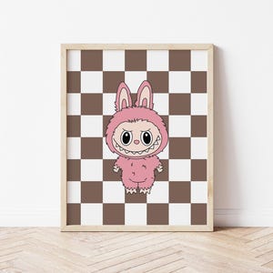 May include: A framed print featuring a cartoon character in a pink bunny costume with a menacing expression. The artwork is set against a brown and white checkered background, framed in a light wood.