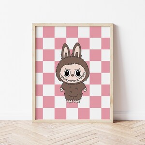 May include: A framed print featuring a cartoon character in a brown bunny costume with a menacing grin. The character stands against a pink and white checkered background. The frame is a light wood color.