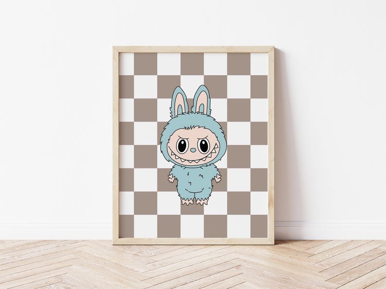 May include: Framed artwork featuring a cartoon monster in a blue bunny costume. The monster has a wide, toothy grin and is set against a brown and white checkered background. The artwork is in a light wooden frame.