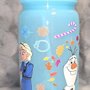May include: A light blue tumbler with a matching lid and straw. The tumbler features illustrations of Elsa and Olaf from the movie Frozen, along with snowflakes, candy canes, and autumn leaves.