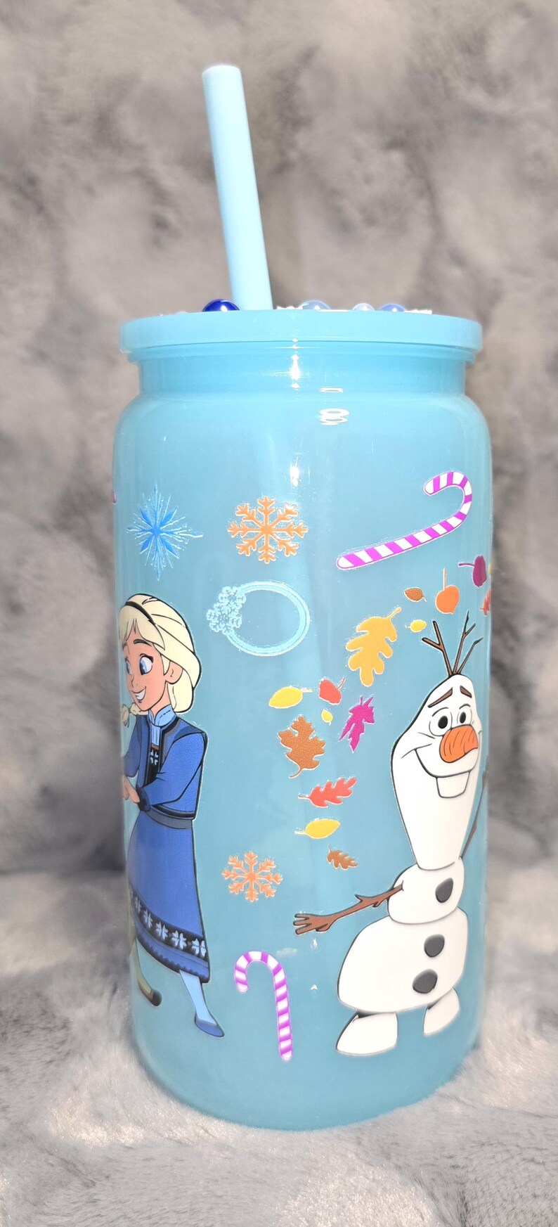 May include: A light blue tumbler with a matching lid and straw. The tumbler features illustrations of Elsa and Olaf from the movie Frozen, along with snowflakes, candy canes, and autumn leaves.