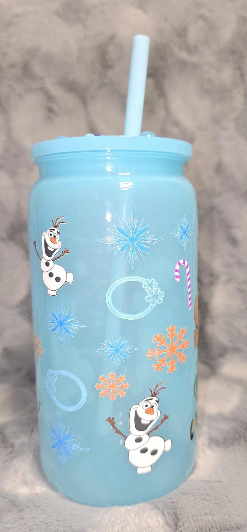May include: A light blue tumbler with a matching lid and straw. The tumbler is decorated with images of Olaf the snowman, snowflakes, and a candy cane. A fun, reusable drinking cup.