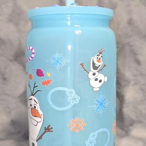 May include: A light blue tumbler with a matching lid and straw. The tumbler is decorated with images of Olaf from the movie Frozen, snowflakes, and other winter-themed graphics. A fun and functional drinkware item.