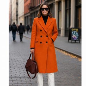 May include: A vibrant orange double-breasted wool coat featuring a notched lapel, six black buttons, and two side flap pockets. The coat is worn over a black turtleneck sweater and white trousers, paired with a structured dark burgundy handbag.
