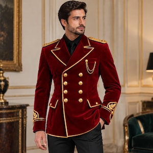 May include: A deep red velvet double-breasted blazer featuring gold piping, gold-tone buttons, shoulder epaulets, and gold embroidered leaf motifs on the cuffs. A gold chain detail is attached to the chest pocket, paired with a black shirt.
