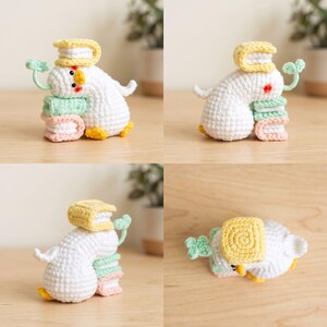 May include: A white crocheted duck figurine with orange feet and beak, featuring pink blush marks. The duck is positioned with a stack of three small crocheted books in yellow, light green, and light pink, and a small green four-leaf clover sprout.