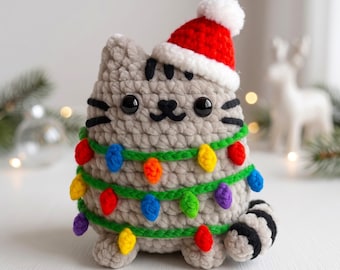 May include: A gray crocheted cat plush toy wearing a red and white Santa hat. The cat is wrapped in a green yarn garland featuring small, colorful, multi-shaped light bulb ornaments in red, blue, orange, yellow, green, and purple hues.