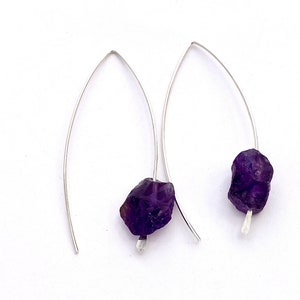 May include: A pair of silver earrings with a raw amethyst stone on each earring.