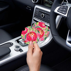 May include: Two round car coasters with a pink and green floral design featuring pomegranates.