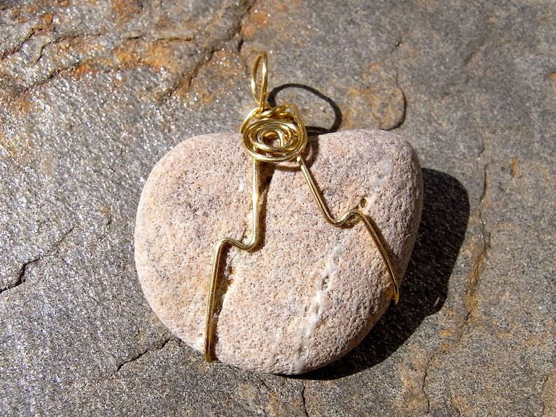 May include: A heart-shaped stone pendant with a gold wire design. The wire is wrapped around the stone and forms a swirl at the top, creating a loop for hanging.