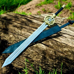 May include: A decorative sword with a silver blade and a gold-colored hilt. The sword rests on a weathered wooden log, with a black sheath beside it. The hilt features intricate detailing, and the handle is wrapped in black material.