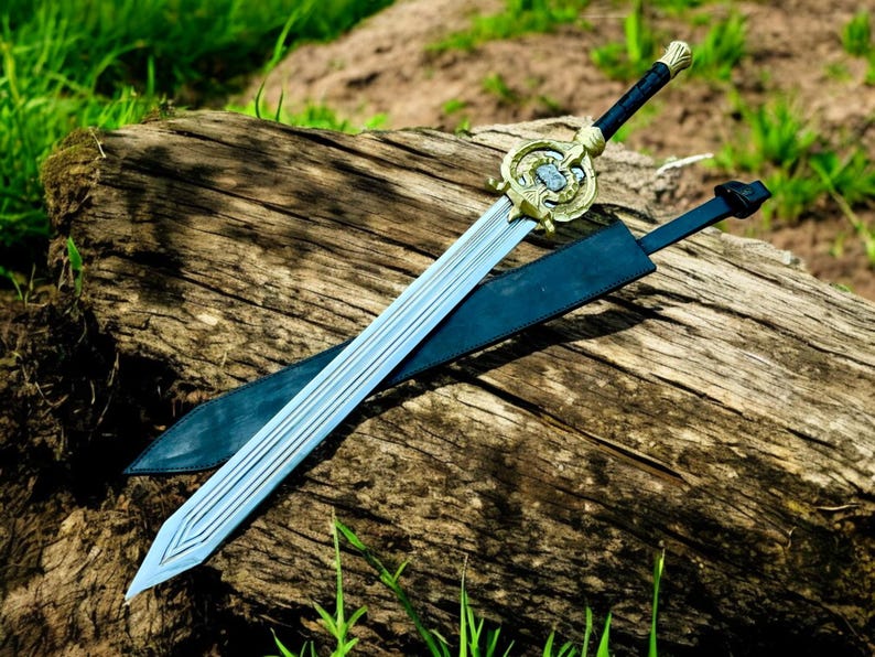 May include: A decorative sword with a silver blade and a gold-colored hilt. The sword rests on a weathered wooden log, with a black sheath beside it. The hilt features intricate detailing, and the handle is wrapped in black material.