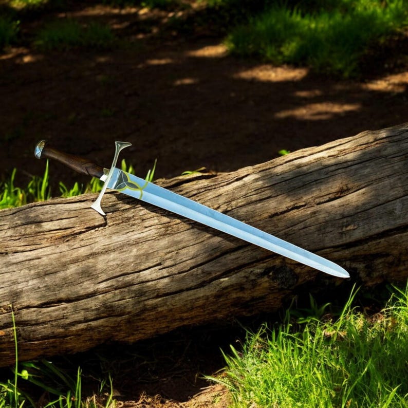May include: A long, silver sword with a polished blade and a dark wooden handle rests on a weathered log. The sword features a decorative hilt with a stylized design and a blue gem at the pommel. The scene is set outdoors with green grass.