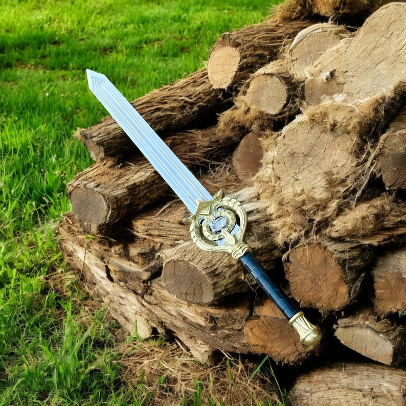 May include: A decorative sword with a light blue blade and a gold-colored hilt. The hilt features an ornate design with a blue gem in the center. The handle is black with gold accents. The sword rests on a pile of wooden logs.
