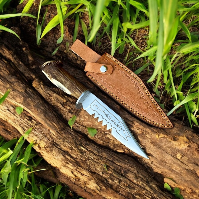 May include: A hunting knife with a wooden handle and a silver blade, resting on a piece of wood. The knife has a serrated edge and is accompanied by a brown leather sheath. The blade has etched text.