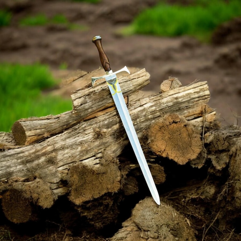 May include: A silver sword with a wooden handle and ornate hilt rests on a pile of weathered logs. The blade is long and pointed, with a decorative emblem near the hilt. The handle is dark brown, and the hilt is silver with gold accents.
