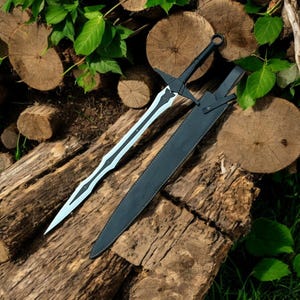 May include: A black and silver sword with a matching black sheath rests on a pile of wooden logs. The sword features a detailed blade design and a black handle. The sheath is made of black leather. The sword is a decorative item.