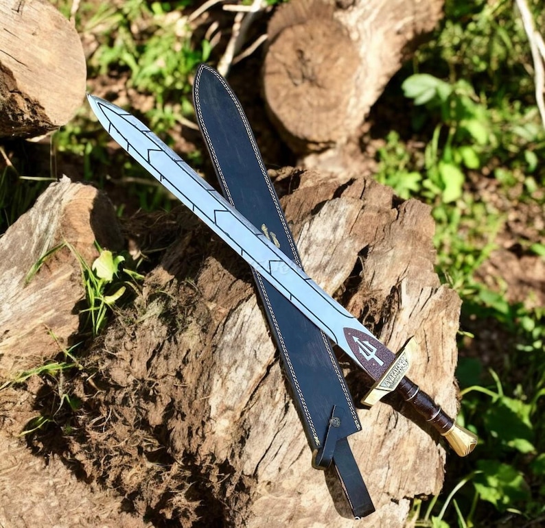 May include: A decorative sword with a light blue blade featuring a geometric design, resting on a black sheath. The hilt is brown with a gold-colored pommel. The sword is displayed on a weathered wooden surface.