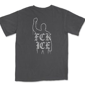 Puede incluir: Camiseta gris oscuro con un gr&aacute;fico blanco en la espalda. El gr&aacute;fico presenta una silueta de pu&ntilde;o en alto con el texto "FCK ICE" en una fuente g&oacute;tica. La camiseta tiene mangas cortas y cuello redondo.